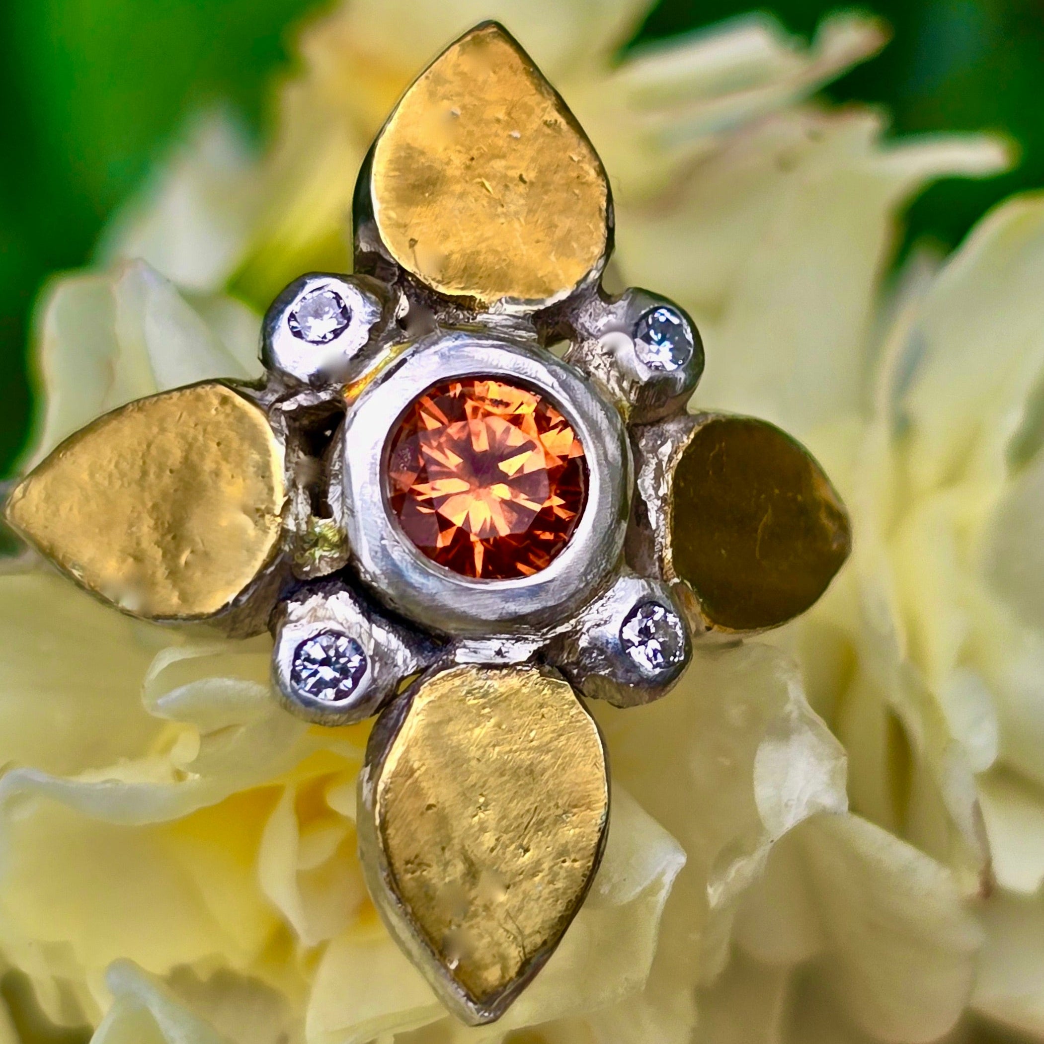 Gold and silver ring with a central orange garnet gemstone with diamonds on a yellow flower background