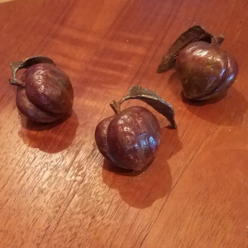 Three painted bronze miniature peaches with a leaf on a wooden background