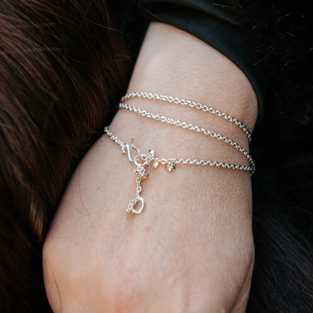 Close-up of a wrist wearing multiple wrapped silver bracelet with flower charms on a dark background.