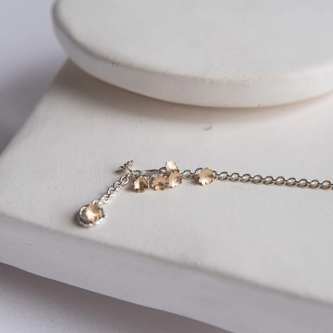 Delicate silver bracelet with small gold flowers on a white surface