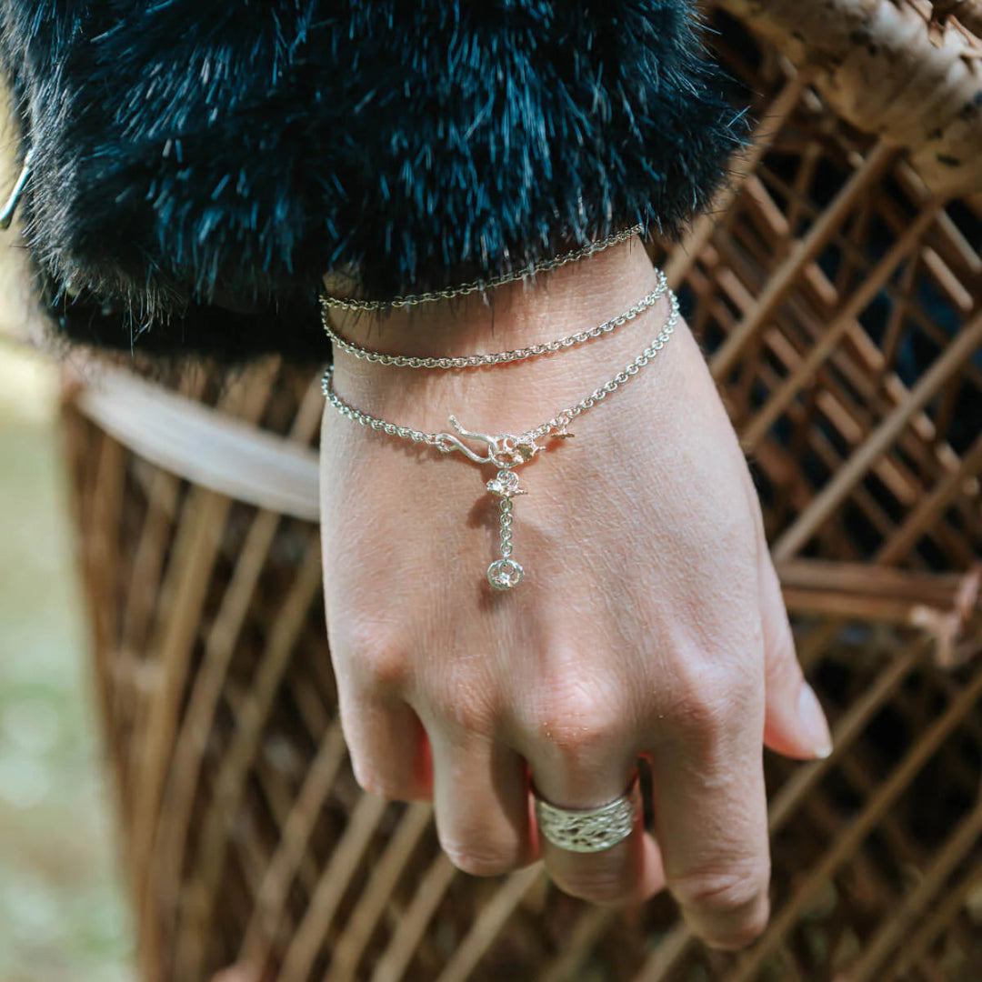 Hand wearing multiple wrapped silver bracelet with a blurred natural background