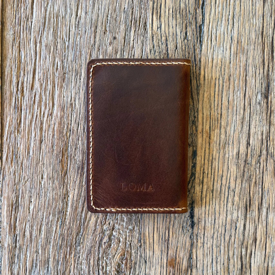 Brown leather wallet with 'LOMA' branding on a wooden surface