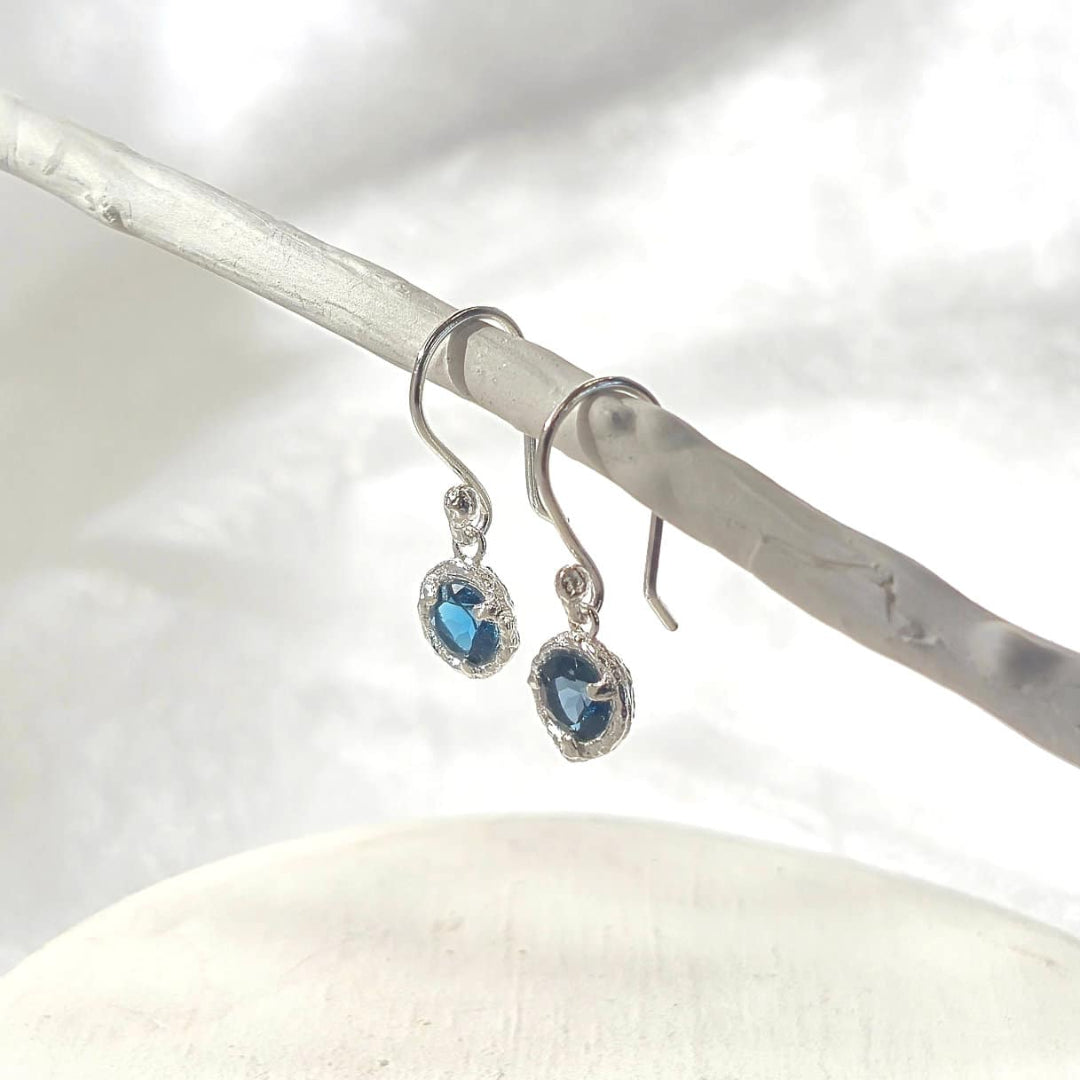 Silver earrings with blue gemstones hanging on a white background