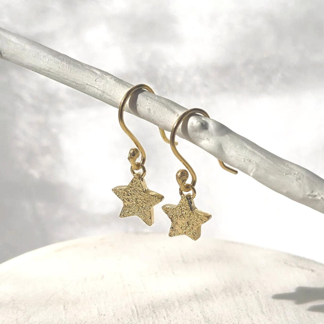 Gold star-shaped earrings on a white stone with a gray background