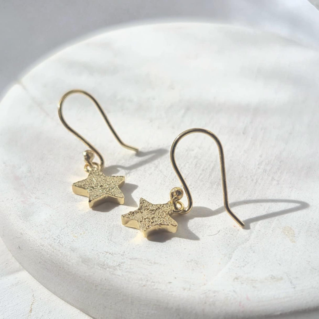 Gold star-shaped earrings on a white stone surface
