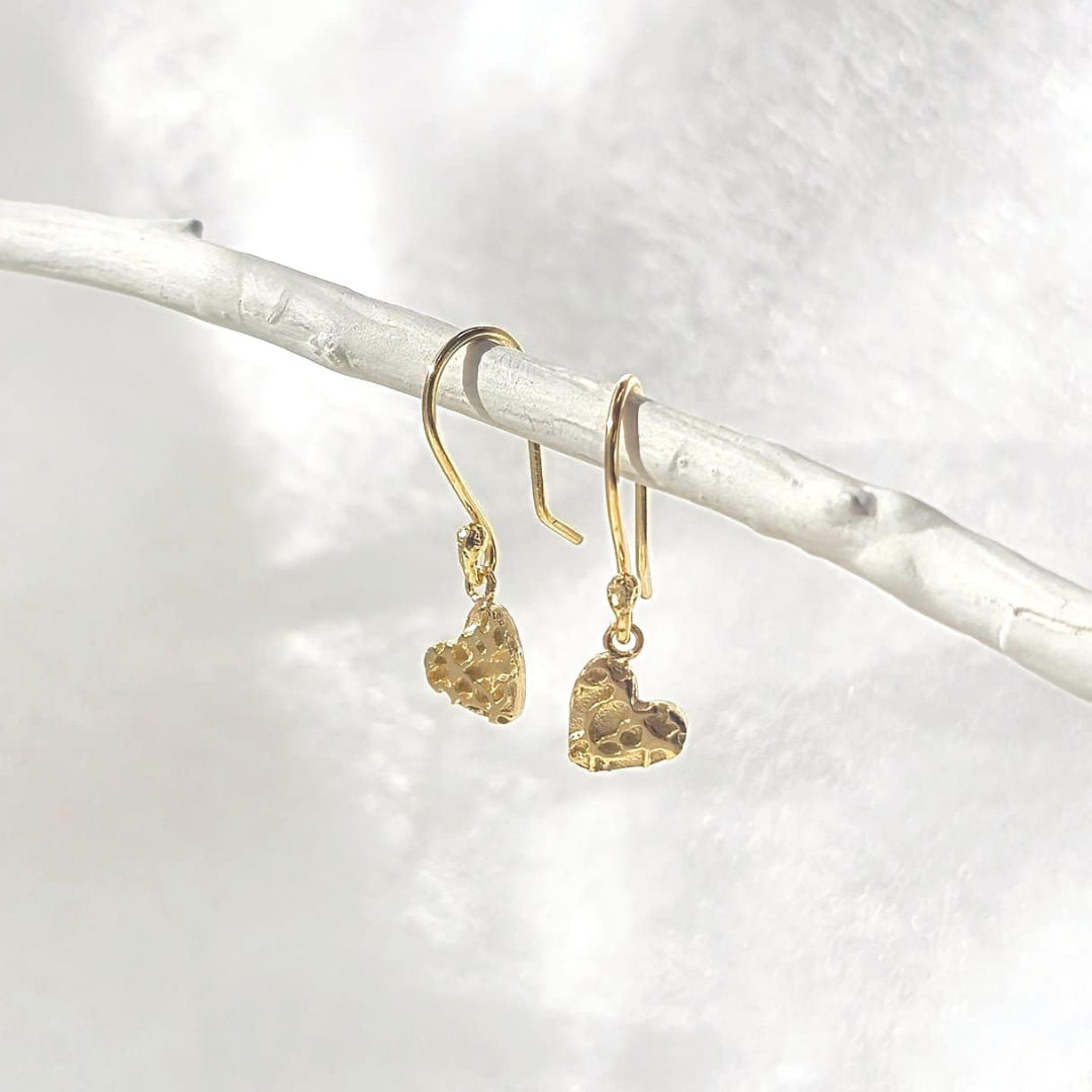 Gold heart-shaped earrings on a white branch with a white background