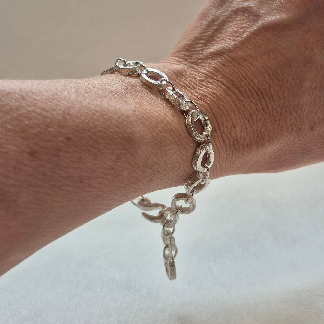 Silver chain bracelet on a wrist with a neutral background