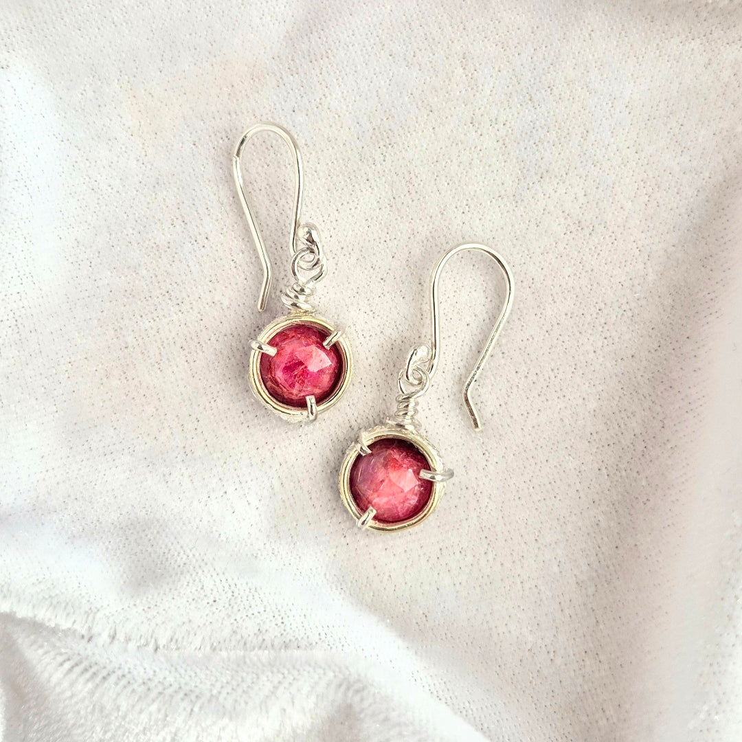 Pair of earrings with pink ruby gemstones on a white fabric background