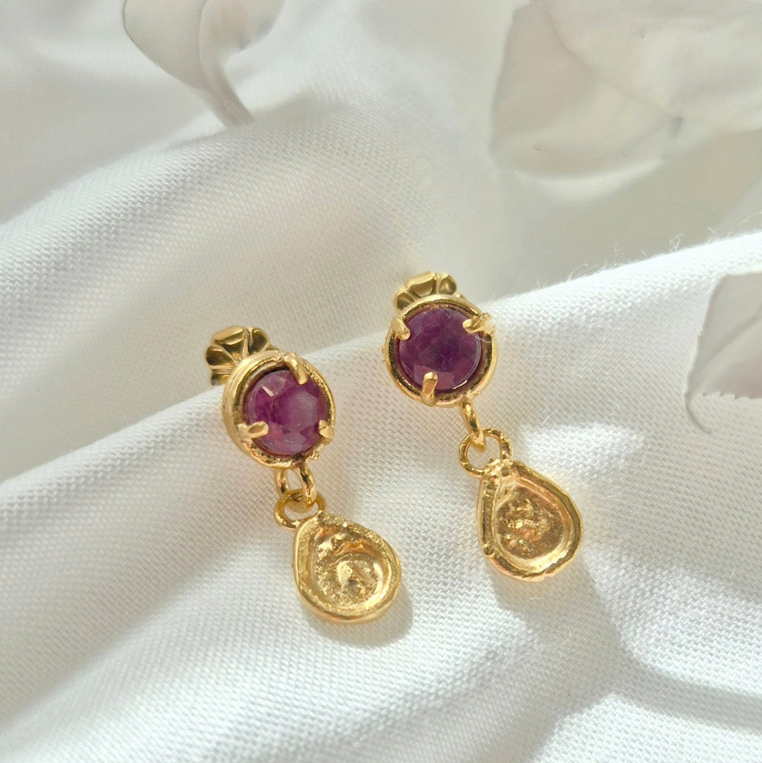 Gold earrings with ruby gemstones on a white fabric background