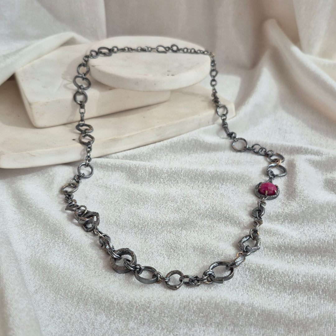 Oxidised silver chain necklace with a pink ruby on a white fabric background