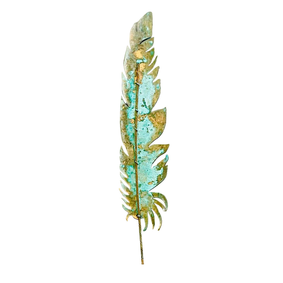 A decorative copper feather wall art piece with a distressed patina showing green verdigris and orange rust-like oxidation, mounted on a white wall.
