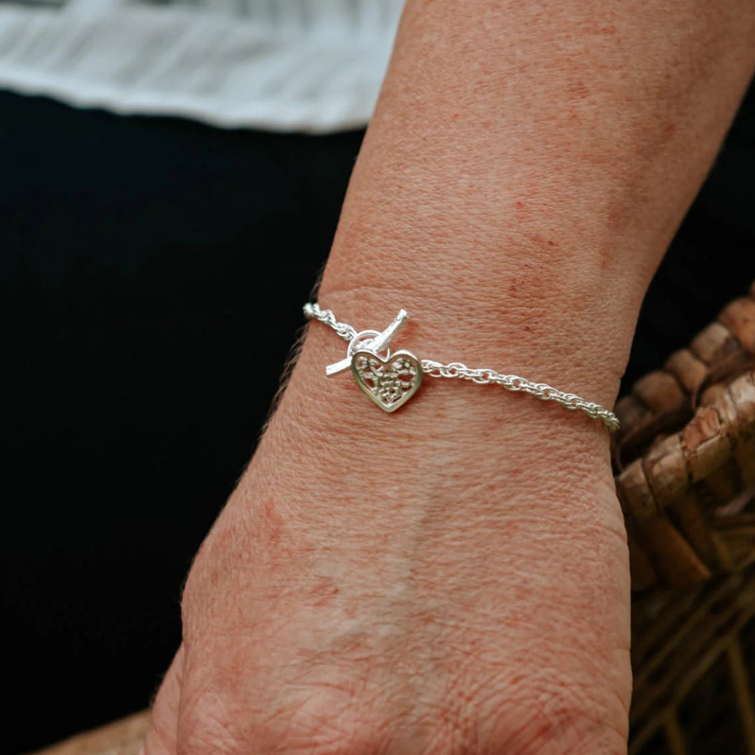 Silver bracelet with a heart charm on a wrist against a blurred background