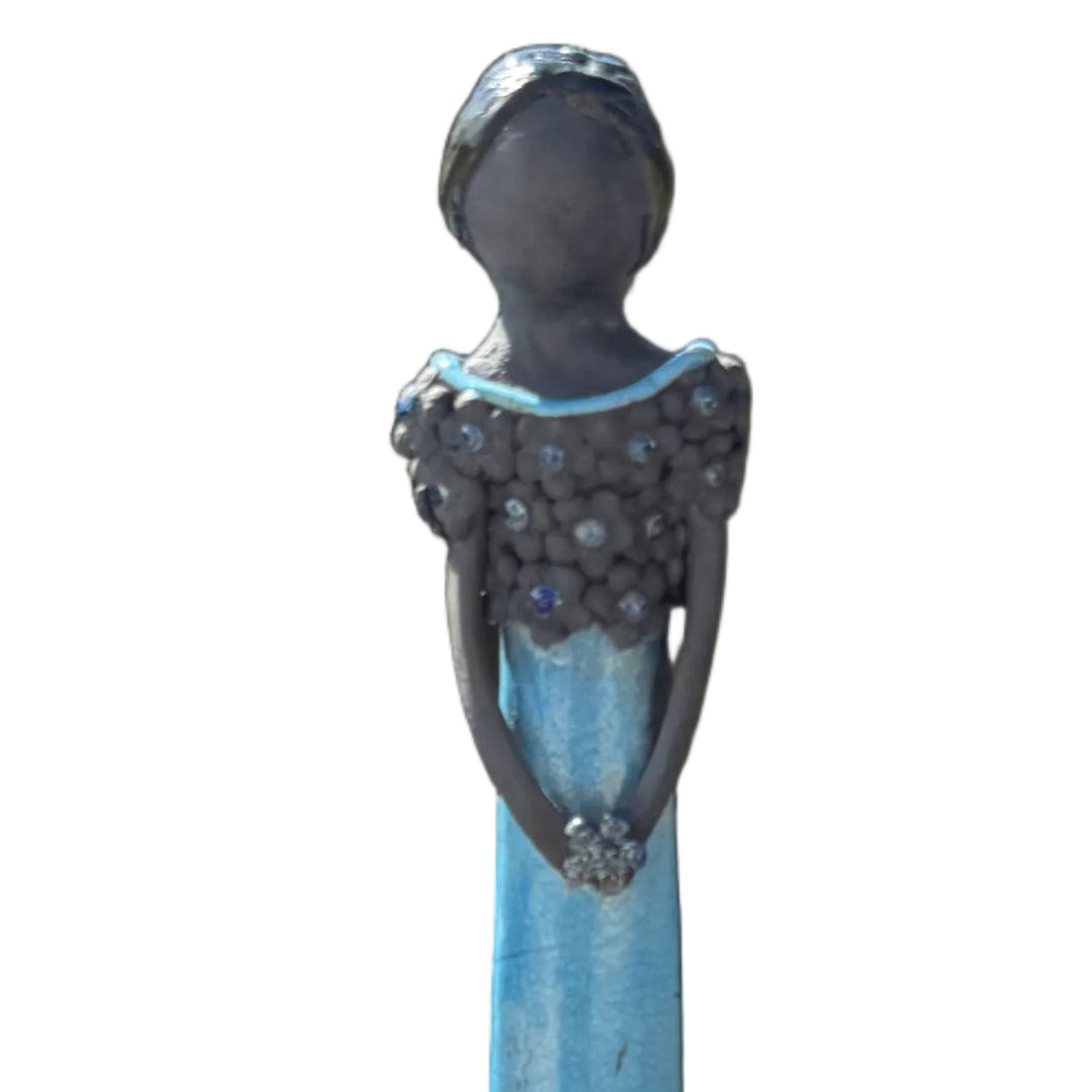 Close up view of a tall lady ceramic figure with an aqua glazed dress & dark floral bodice, holding a silvery flower against a white background.