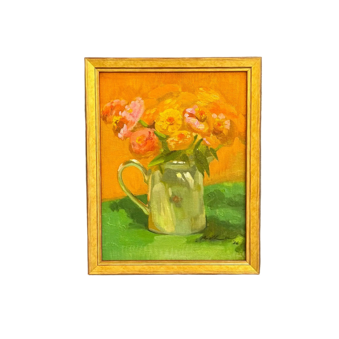 A small framed painting of a green mug filled with pink and yellow flowers against a bright orange background, on a white wall.