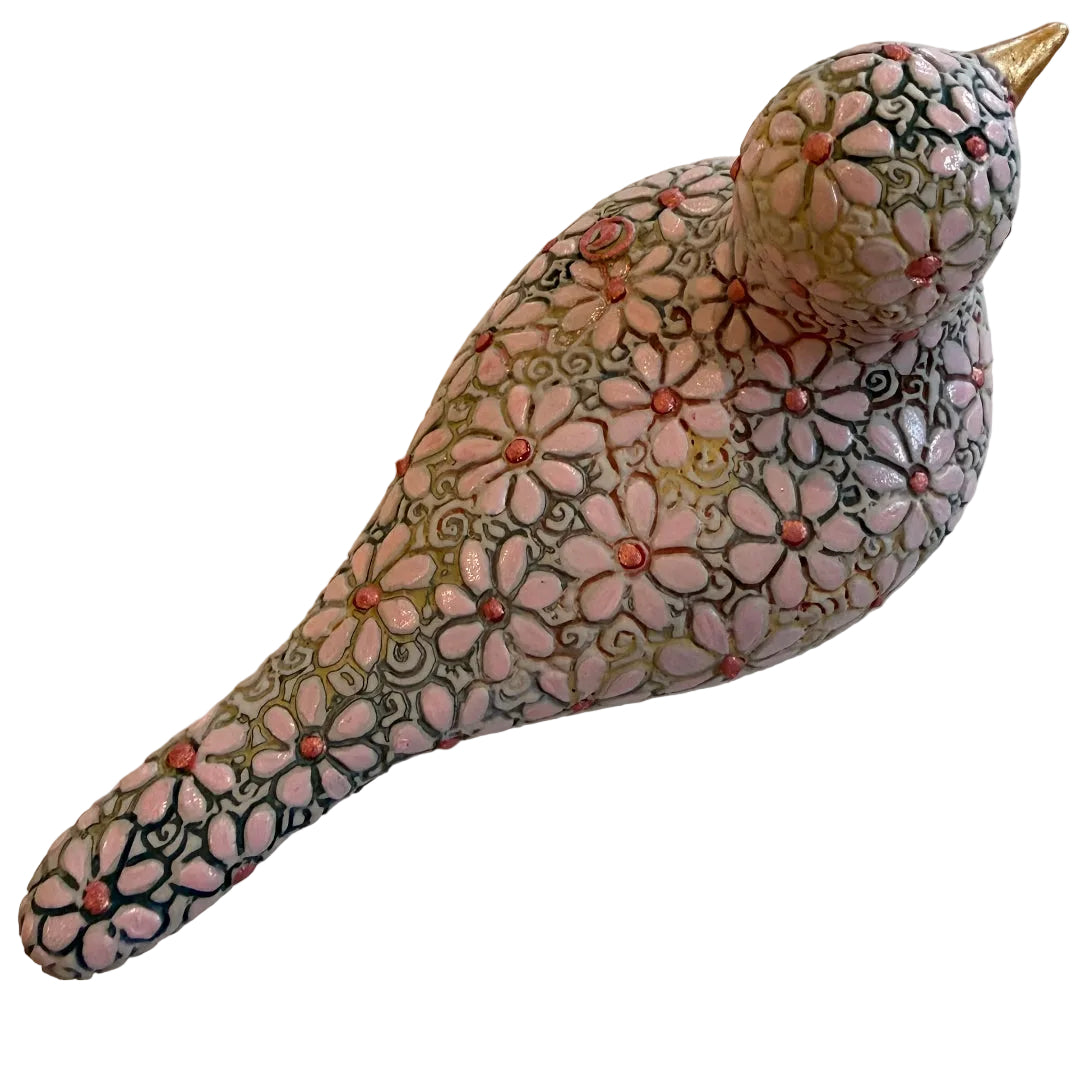 A decorative ceramic bird figurine with a pink and green floral pattern and a gold beak, photographed on a white surface.