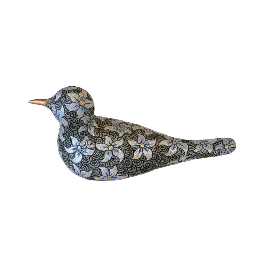 A decorative bird figurine with a black and white floral pattern, light blue flower accents, and a copper-colored beak, resting on a plain white surface.