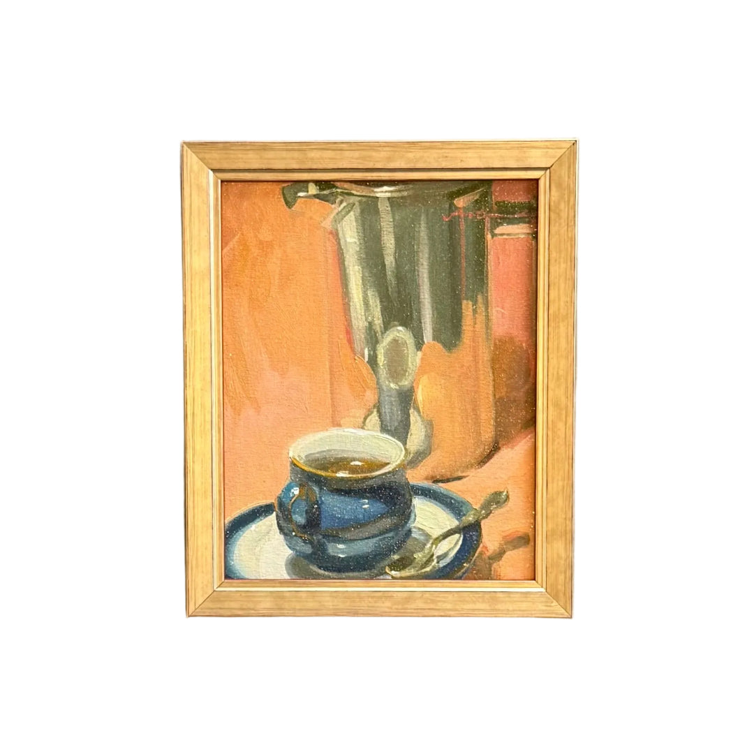 A small framed painting of a blue coffee cup and saucer with a glass on a warm orange background, mounted on a white wall. 