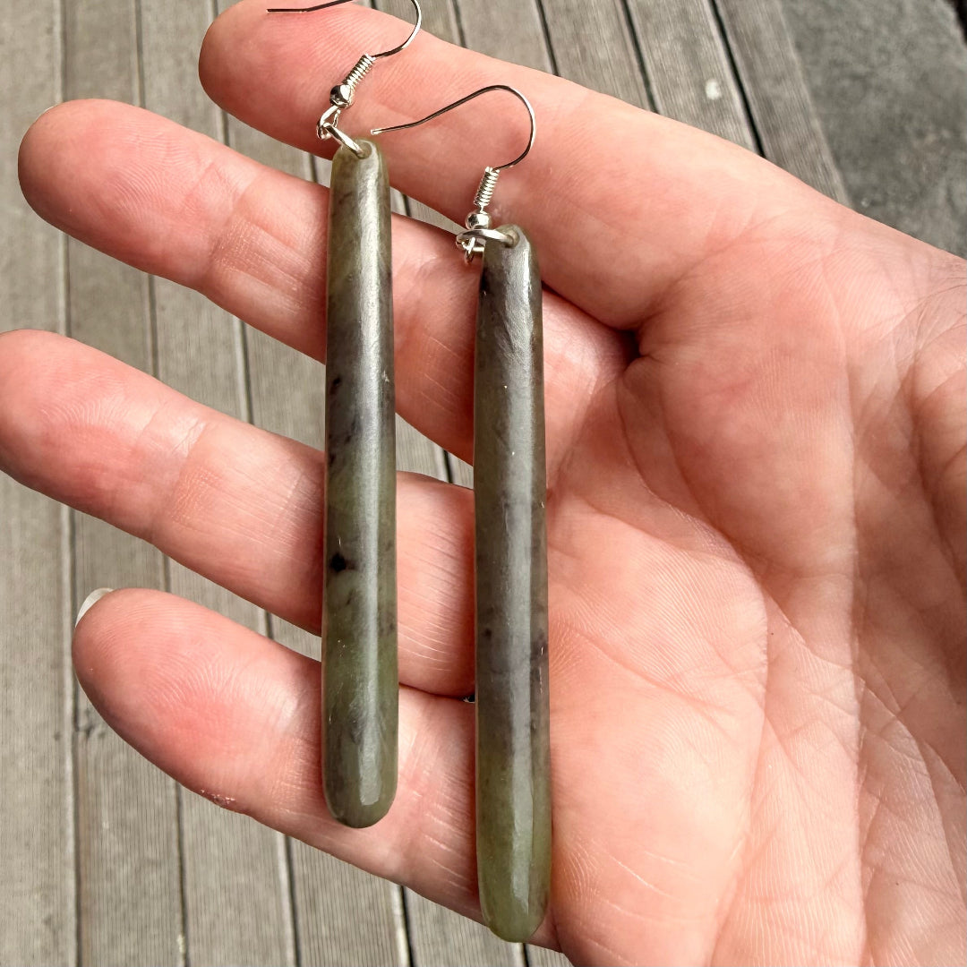 Slender pounamu NZ greenstone earrings held in a hand.