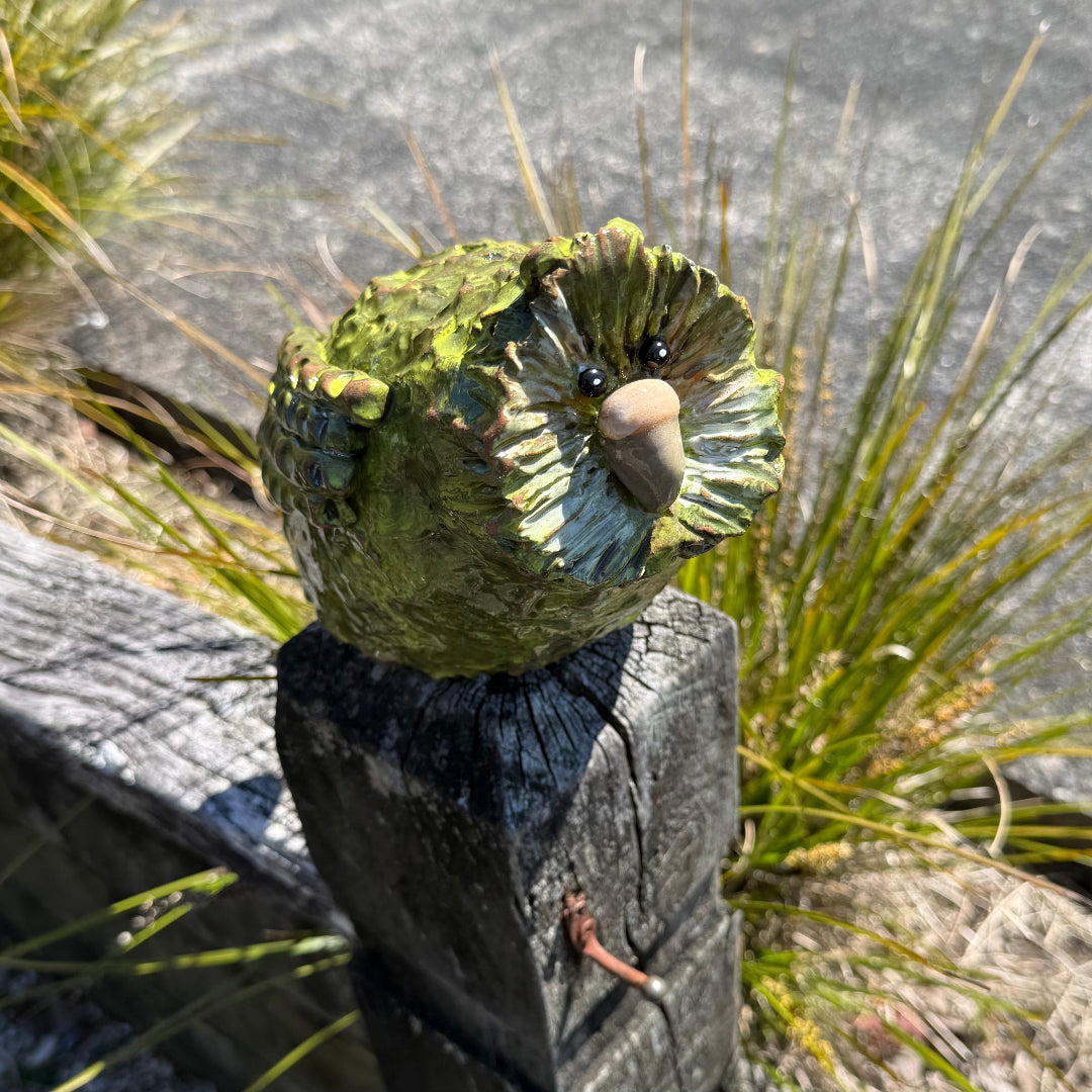 Green pottery Kakapo bird crouching on a post in a garden.