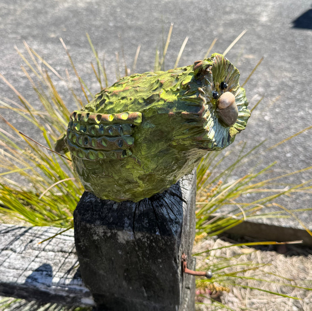 Green pottery Kakapo bird crouching on a post in a garden.