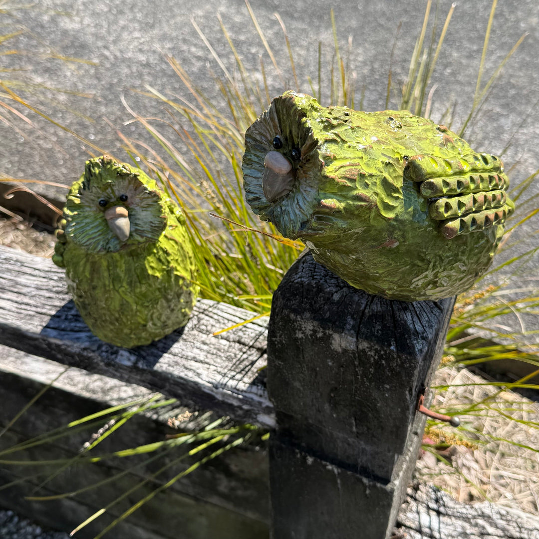 Pair of green pottery Kakapo birds on a post in a garden.