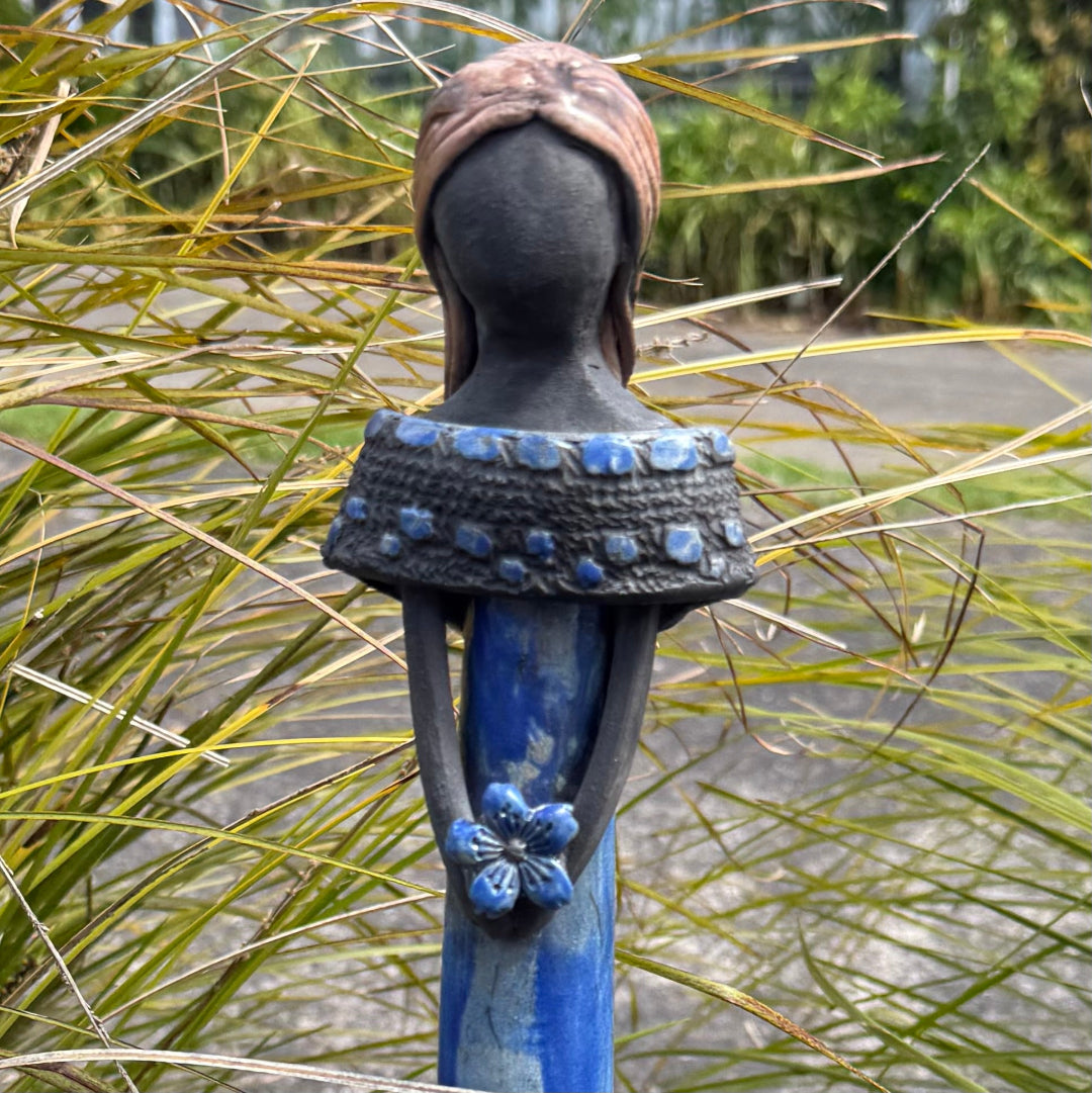 Close up view of a decorative figurine of a woman with light hair, wearing a long blue  dress and holding a blue flower.
