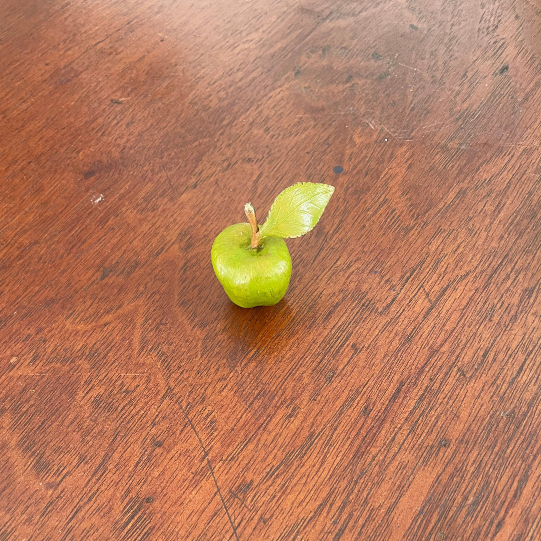 Painted bronze miniature green apple with leaf on a wooden table.
