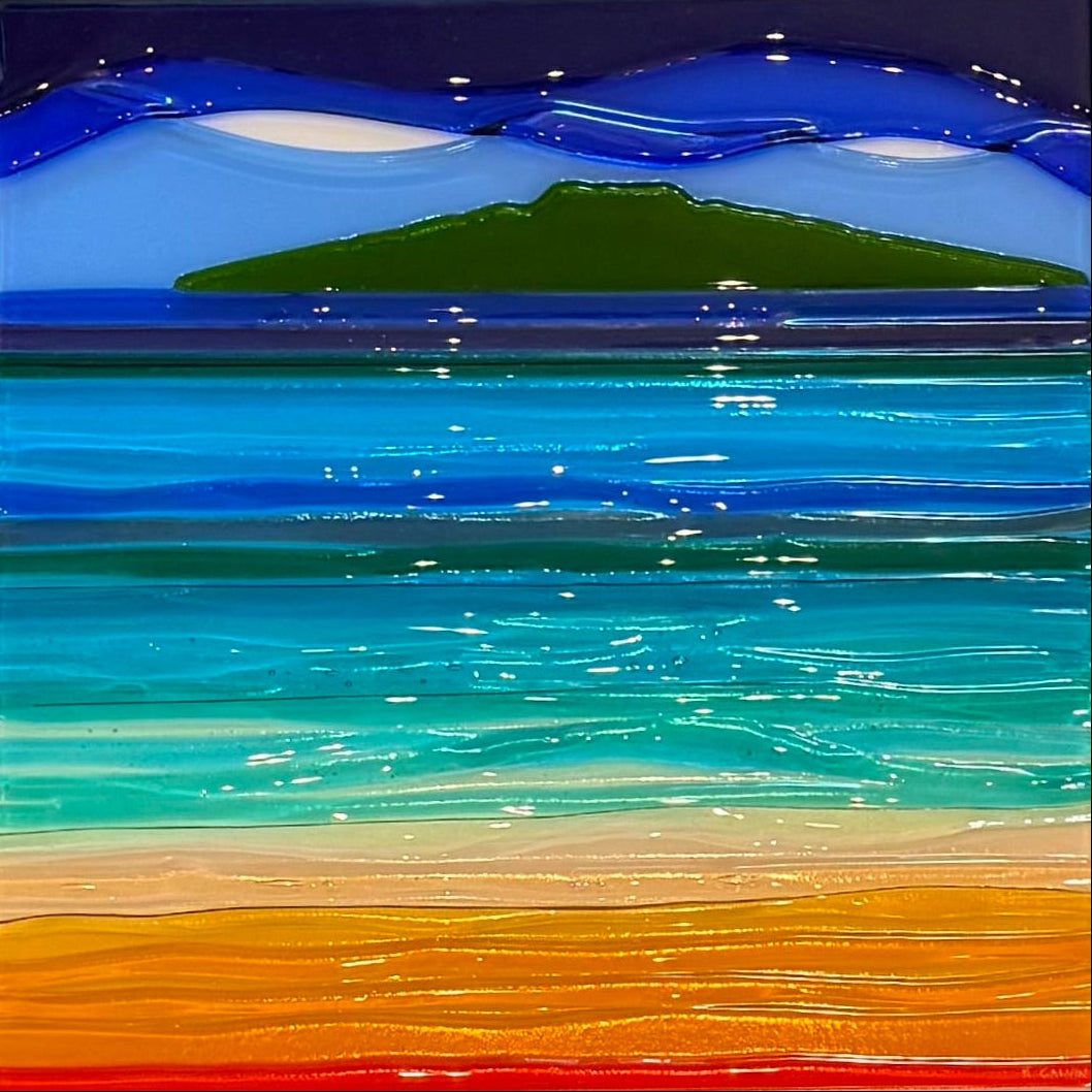 A square framed artwork on a gray wall, featuring a colorful beach and ocean scene with blue water, green island, and orange sand, surrounded by a white frame.