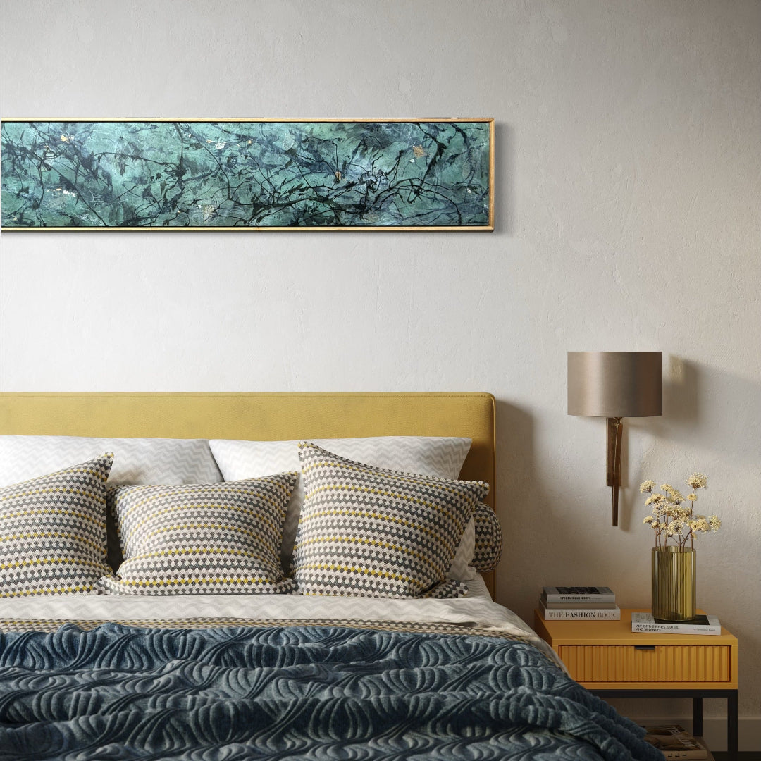A modern bedroom scene featuring a wide horizontal abstract painting with teal, green, and gold brushstrokes on a textured off-white wall above a bed with a mustard yellow headboard, patterned pillows, and a dark blue wavy-patterned quilt.