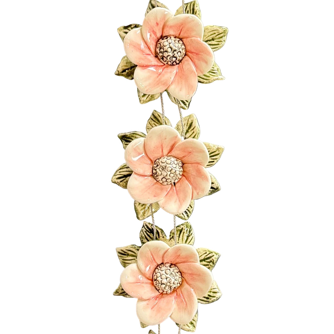 Decorative wall hanging with ceramic pink flowers and green leaves on a white background