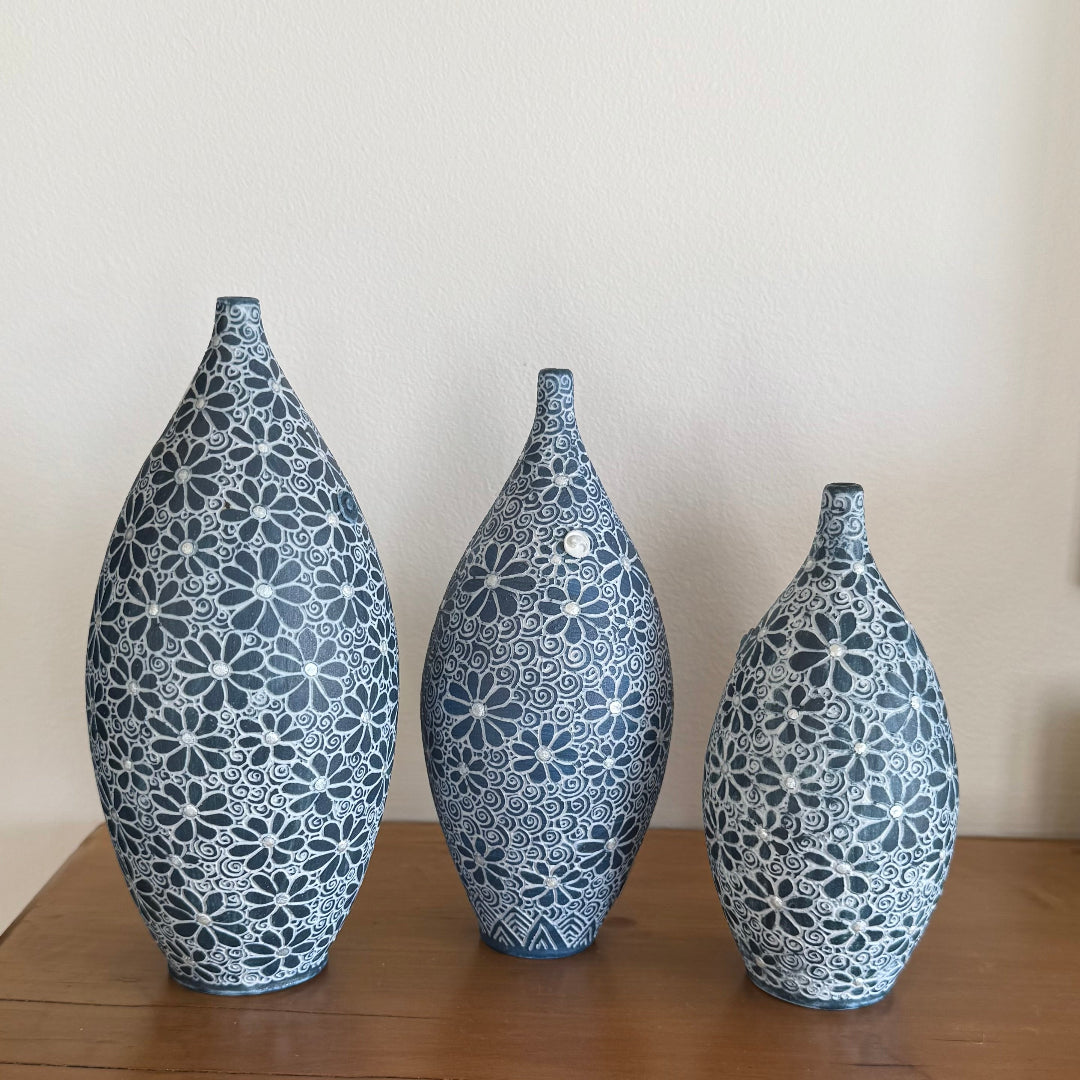Three decorative ceramic bottle vases with carved floral patterns on a wooden surface and beige background