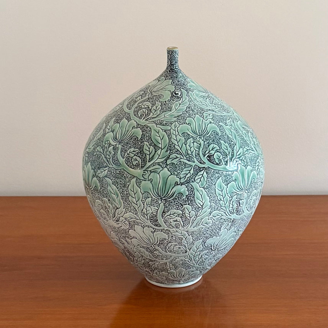Decorative pale green ceramic vase with intricate floral patterns on a wooden surface