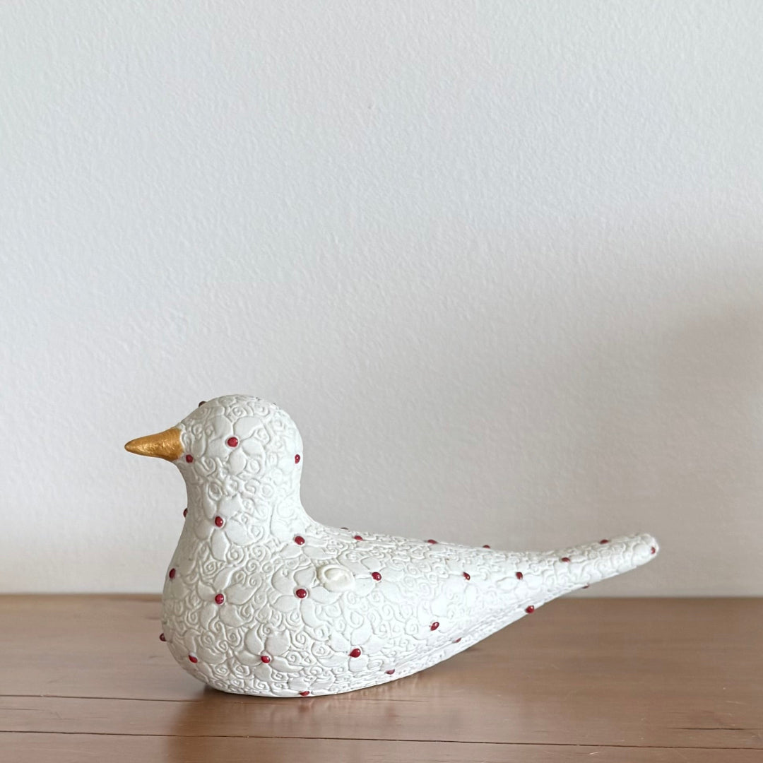 Decorative ceramic white bird figurine with red spots on a wooden surface and cream background
