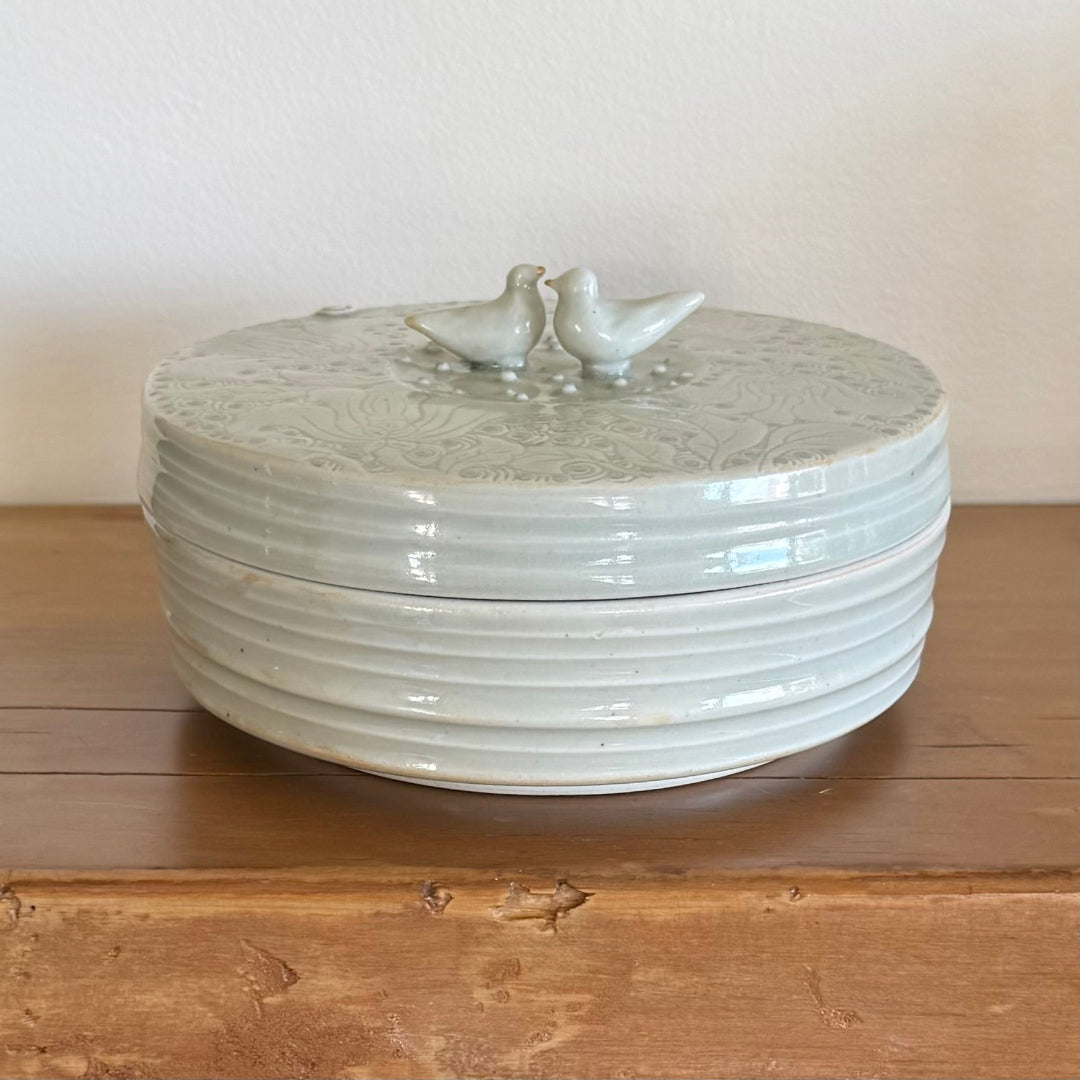White ceramic lidded container with 2 birds on a wooden surface