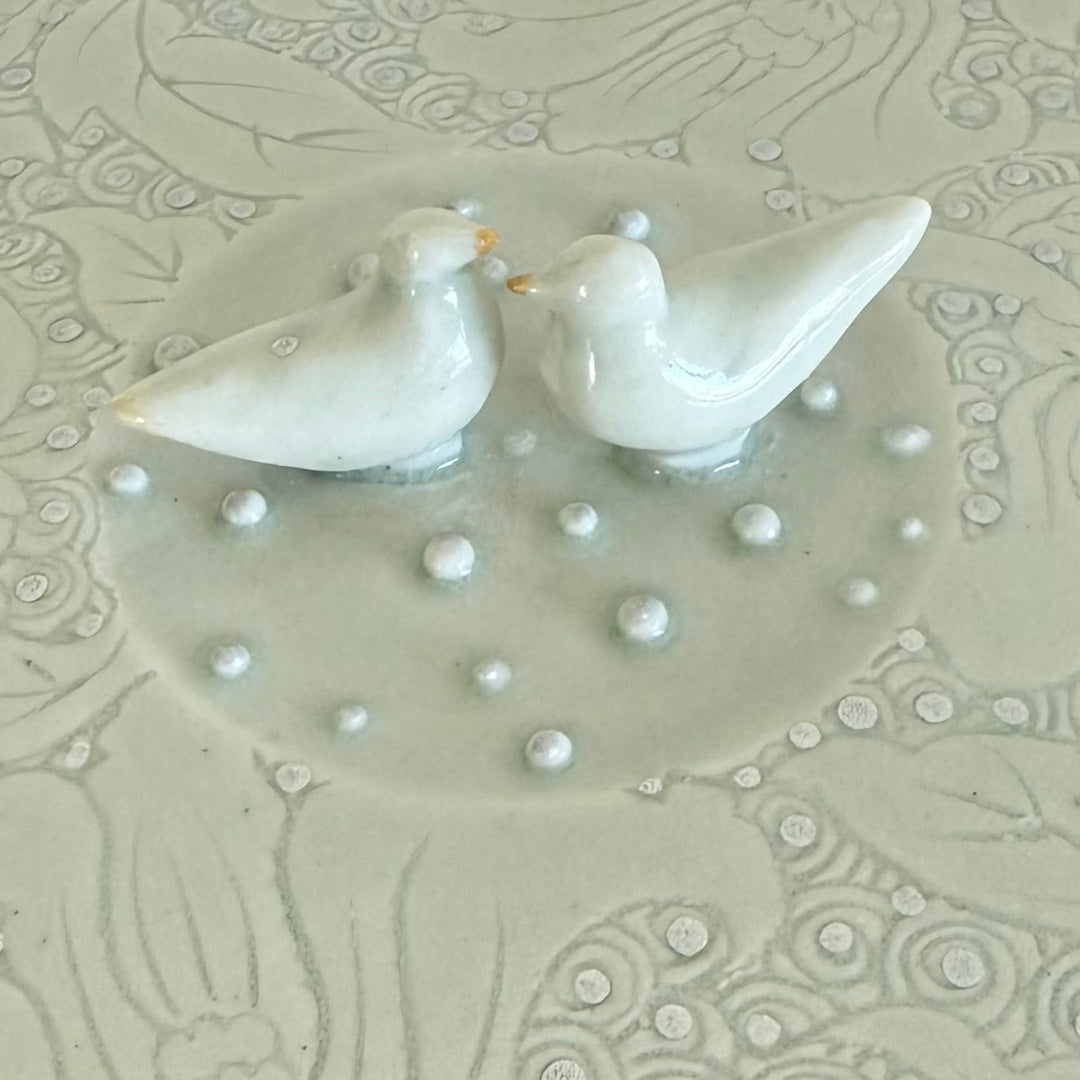 Two white ceramic doves on a textured surface with pearl-like beads.