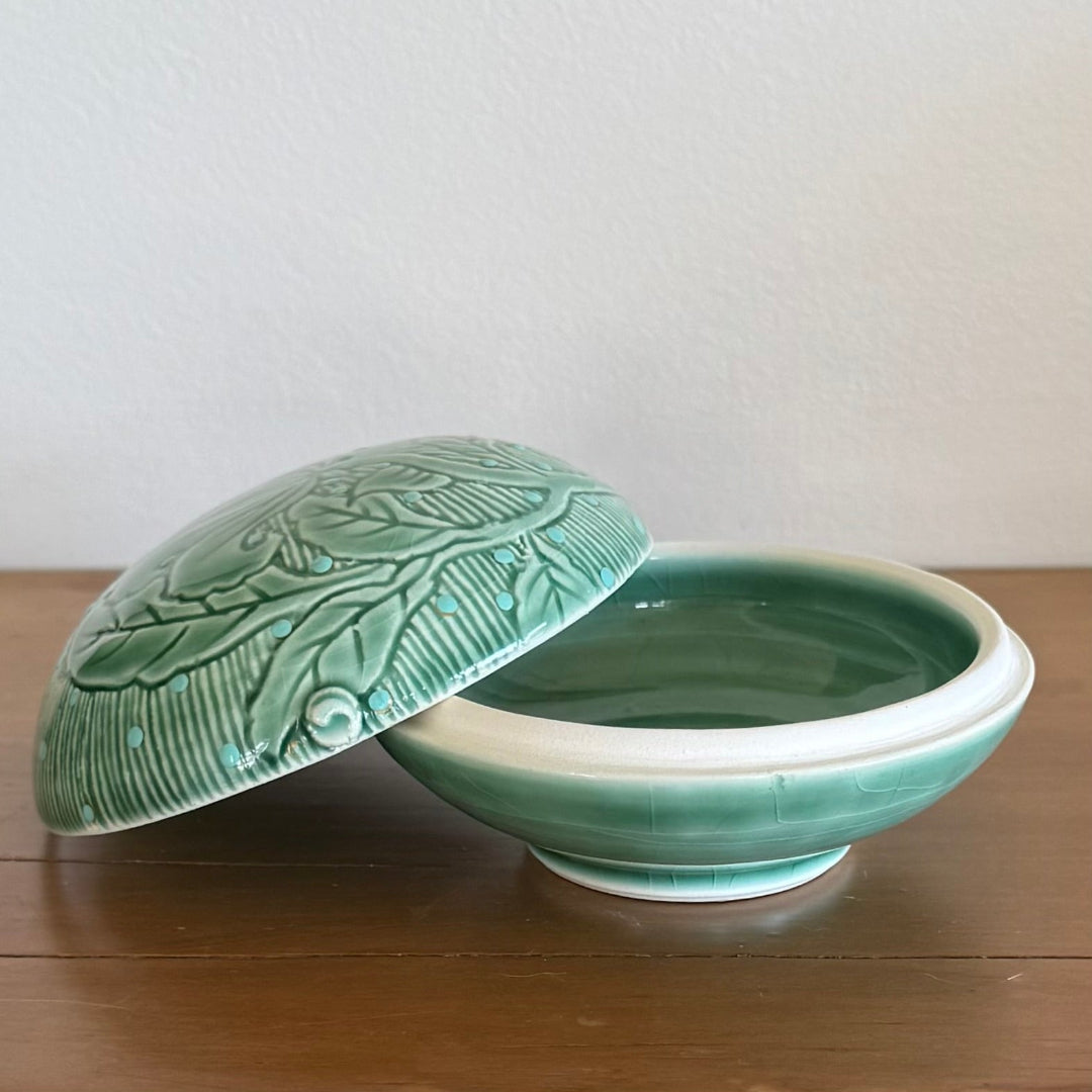 Green ceramic lid and bowl set on a wooden surface with a white background
