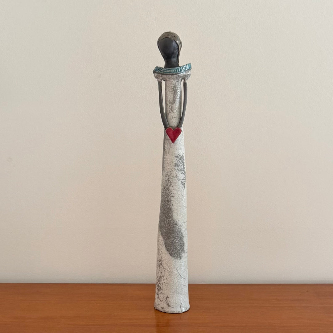 Ceramic sculpture of a figure with a heart on a wooden surface