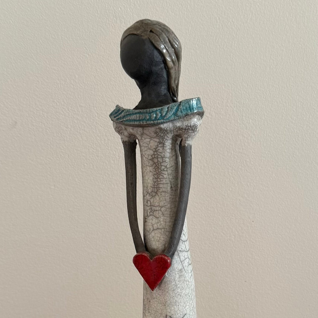 Ceramic sculpture of a figure with a red heart on a plain background