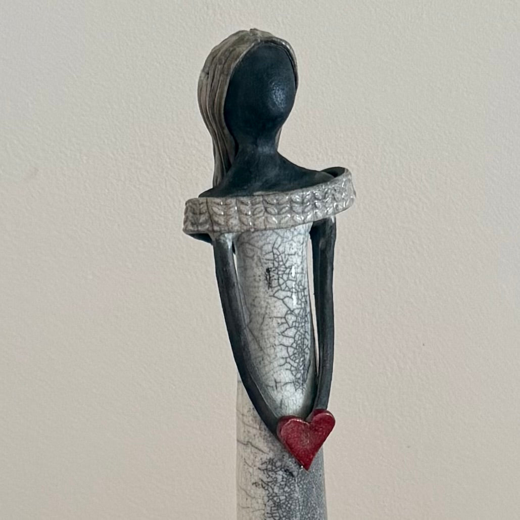 Sculpture of a ceramic figure holding a red heart against a plain background