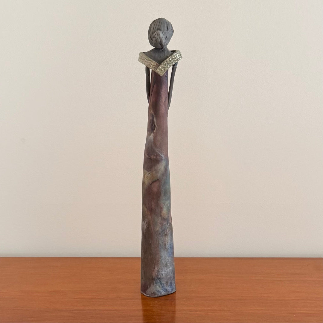 Decorative ceramic sculpture of a woman on a wooden surface with a plain background