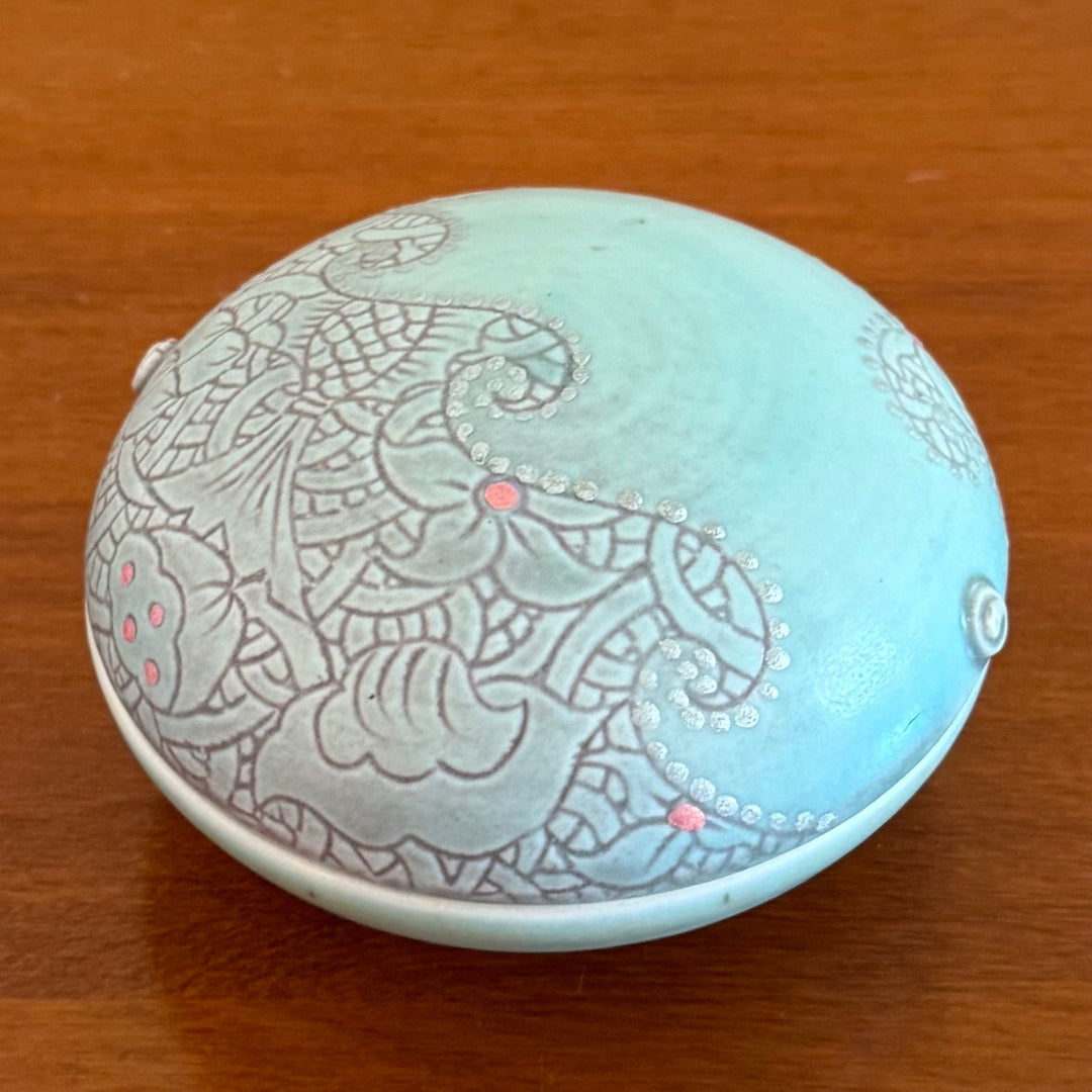 Round ceramic lidded dish with intricate wave patterns on a wooden surface
