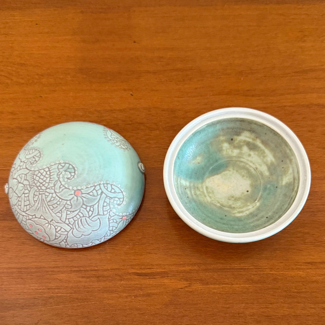 Decorated ceramic lid and dish side by side on a wooden surface.