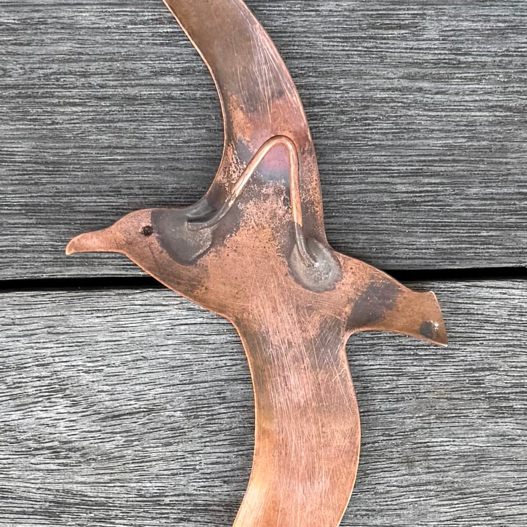 Back view showing hook on a copper Albatross bird sculpture on a wooden surface