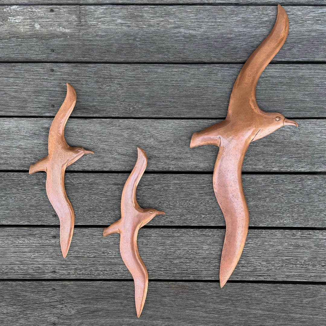 Three copper Albatross bird sculptures on a wooden surface