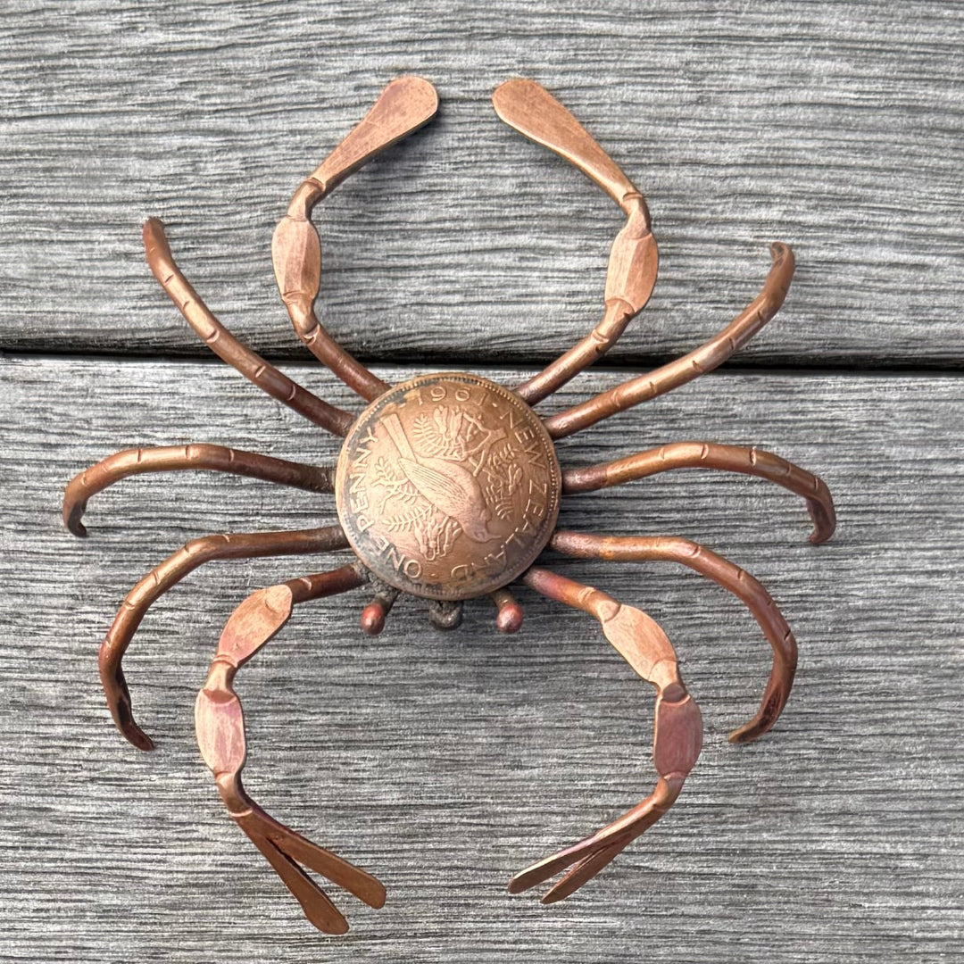 Copper crab sculpture with a coin in the center on a wooden surface