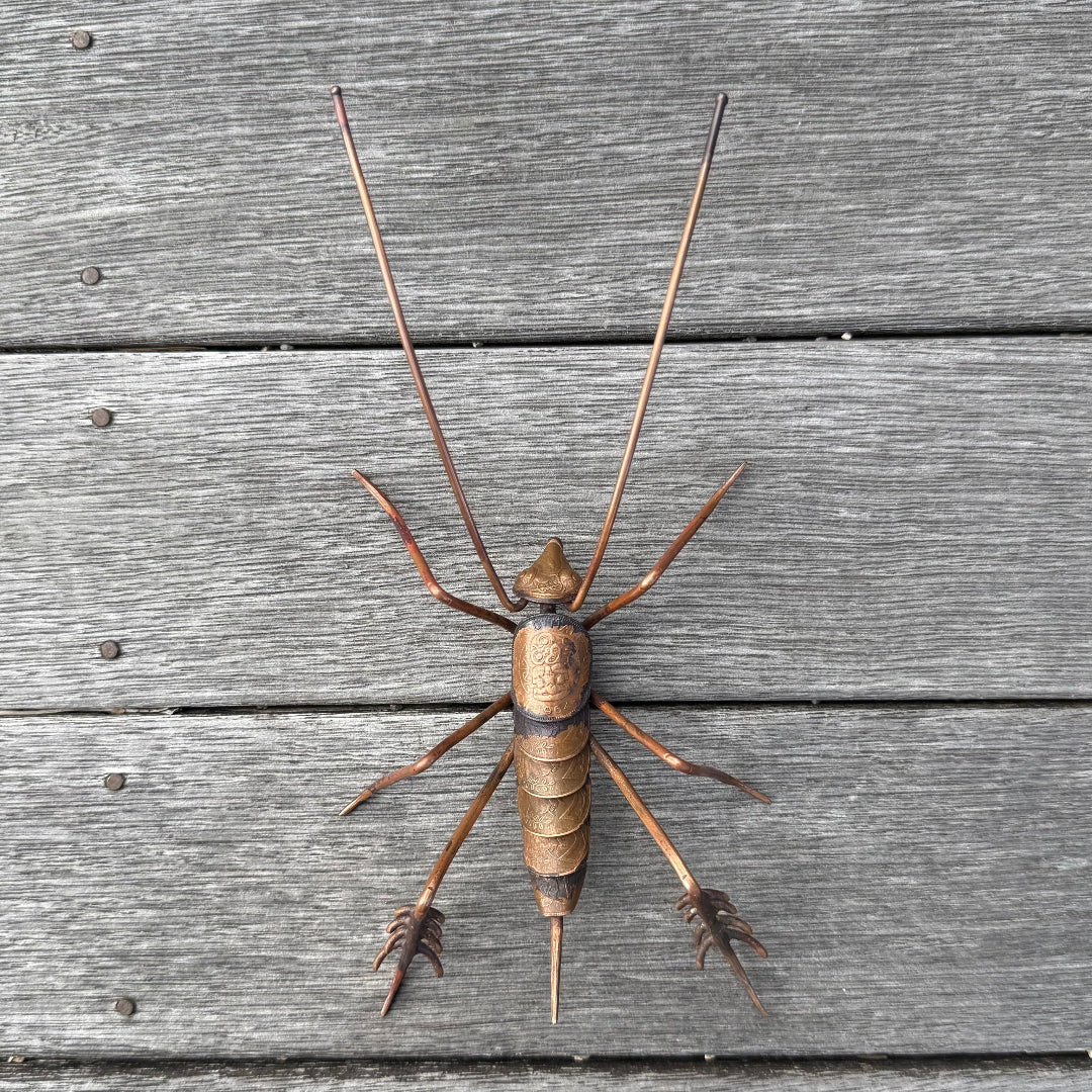 Copper sculpture of a Weta on wooden planks