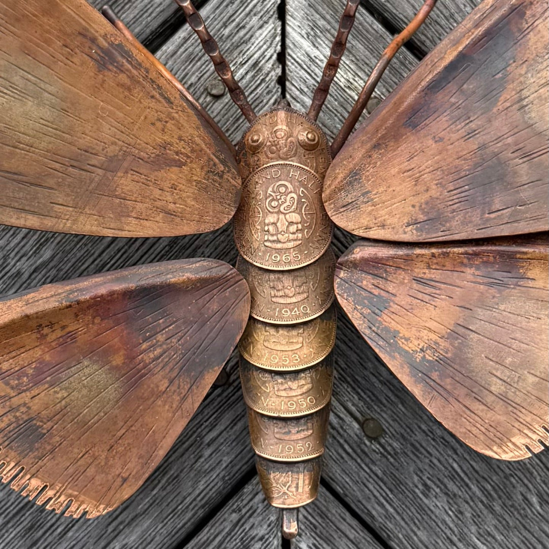 Decorative copper butterfly with coins for body on a wooden surface