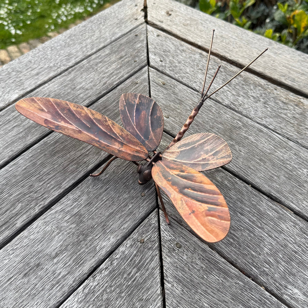 Decorative copper Mayfly sculpture on a wooden surface