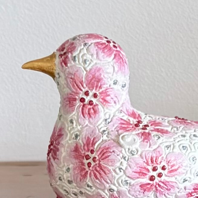 Decorative ceramic bird figurine with floral pattern on a wooden surface