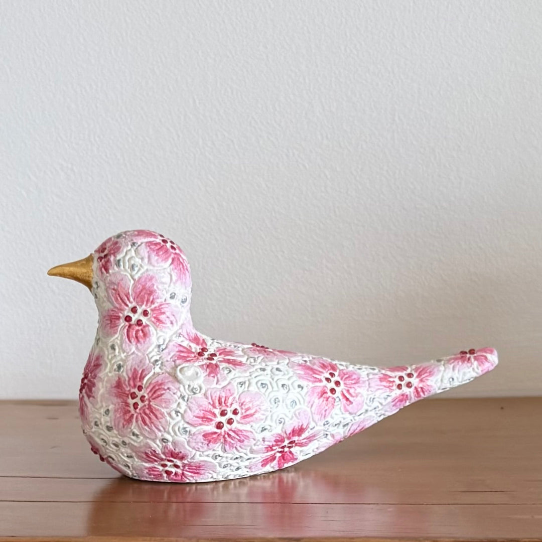 Decorative ceramic bird figurine with floral pattern on a wooden surface